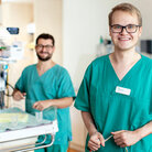 Zwei Männer in türkisenem Kasack an Baby Intensivbett