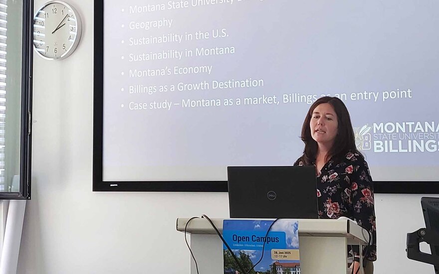 Gastprofessorin steht am Rednerpult vor der Leinwand