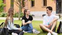 Drei Studierende sitzen auf der Campus Wiese und unterhalten sich