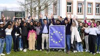Gruppe der Studierenden mit Gastreferent, EU-Schild und alle heben die Hände