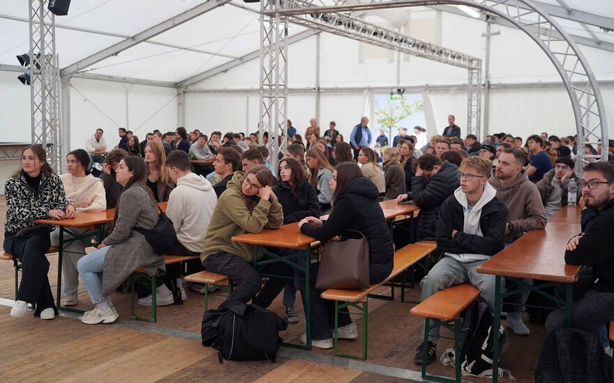 Neue Studierende sitzen an Bankgarnituren im Zelt