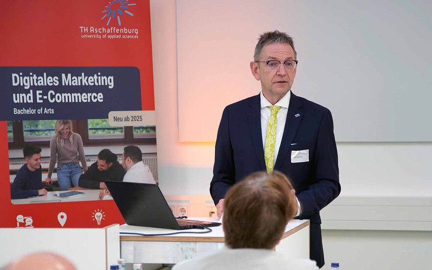 Bürgermeister Kahlert spricht neben einem rot-blauen Studiengangsrollup zu den Gästen