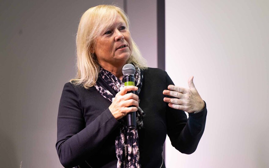 Frau mit blonden Haaren spricht gestikulierend mit Mikrophon in der Hand