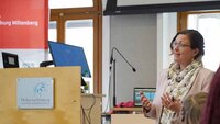 Professorin Bertels spricht am Rednerpult mit TH-Logo in der Aula, rotes Sparkassen-Roll-up dahinter