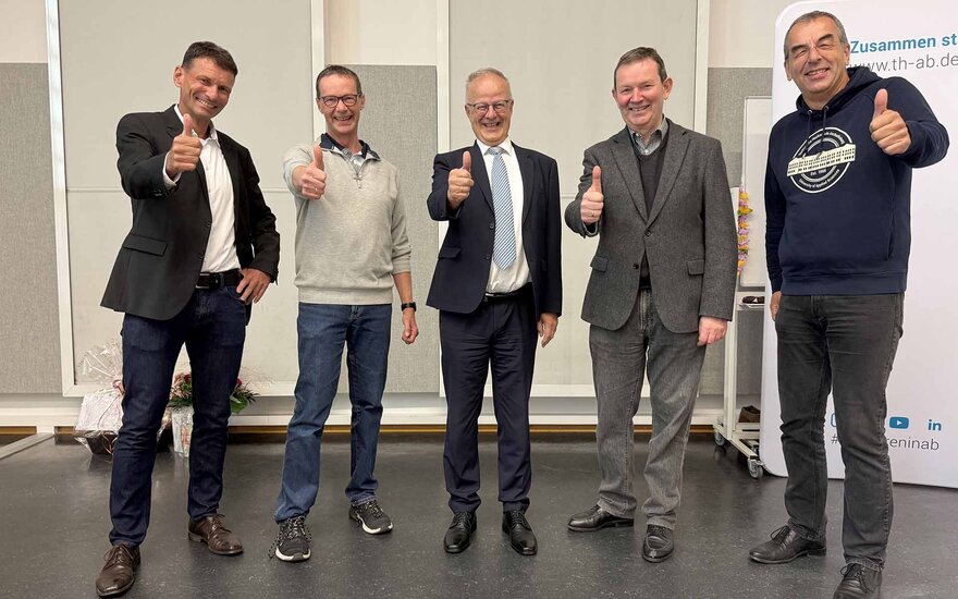 Fünf Männer stehen nebeneinander, lachen und heben den Daumen