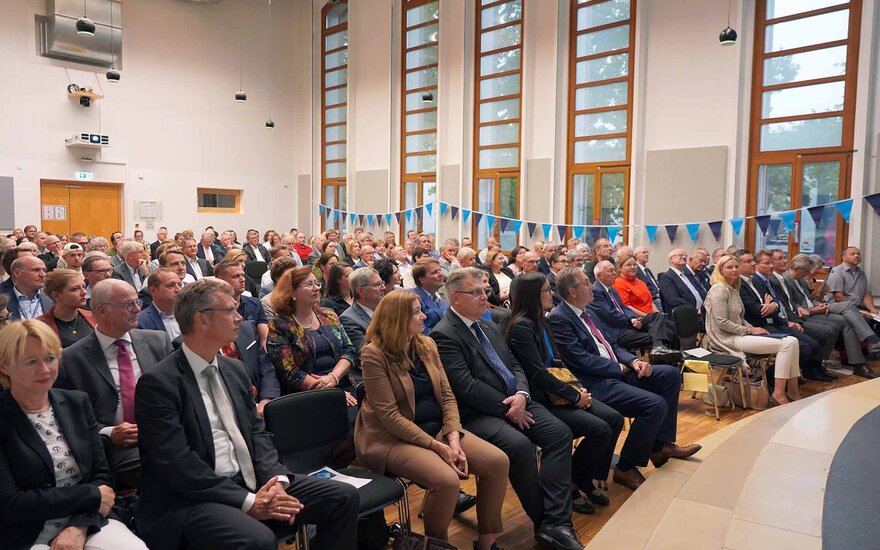 Festpublikum sitzend in Stuhlreihen in der vollbesetzten Aula