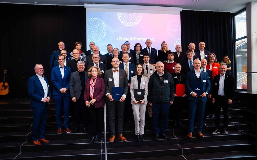 Gruppenbild von mehreren Männern und Frauen vor einer Leinwand mit dem Schriftzug: #ZukunftPromoviert