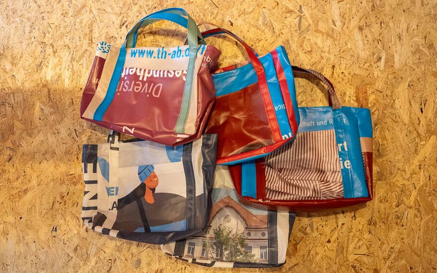 Upcycling-Produkte der TH Aschaffenburg: Taschen, die aus alten Werbebanner bestehen auf einem Korkhintergrund.