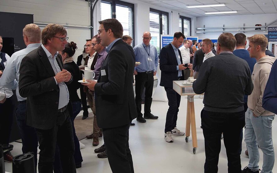 Ein Raum in dem sich viele Menschen in Hemden oder Anzügen unterhalten.