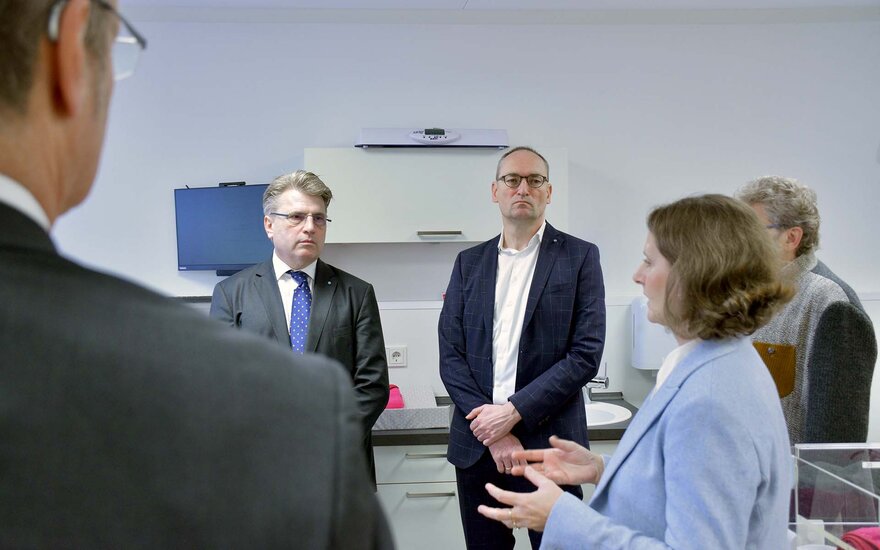 Bausback und Seidenath stehen neben der Professorin im Vorlesungsraum vor einem Bildschirm