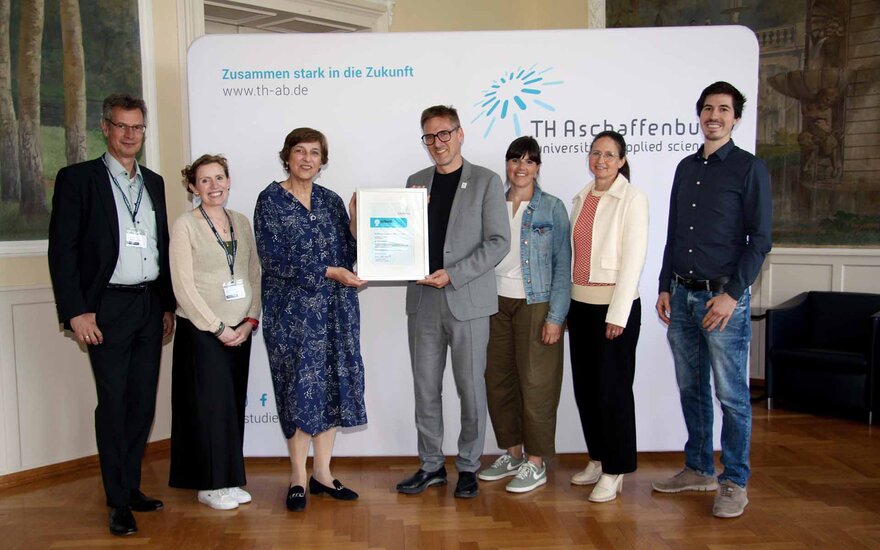 Gruppenfoto vor TH-Logo-Wand im Hocksaal mit drei Männern und drei Frauen