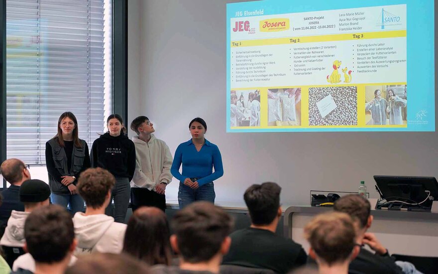 Drei Schülerinnen und ein Schüler präsentieren ihr Projekt vor dem Publikum.
