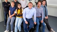 Das Team des Open Innovation Lab lehnt an einem Tisch mit Professor Hellmann in der Mitte