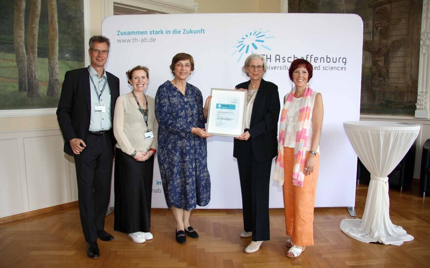 Gruppenfoto vor TH-Logo-Wand im Hocksaal mit einem Mann und vier Frauen