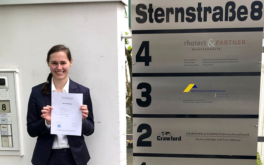 Steuerberaterin Sabrina Maier hält eine Bescheinigung vor einem Adressschild 