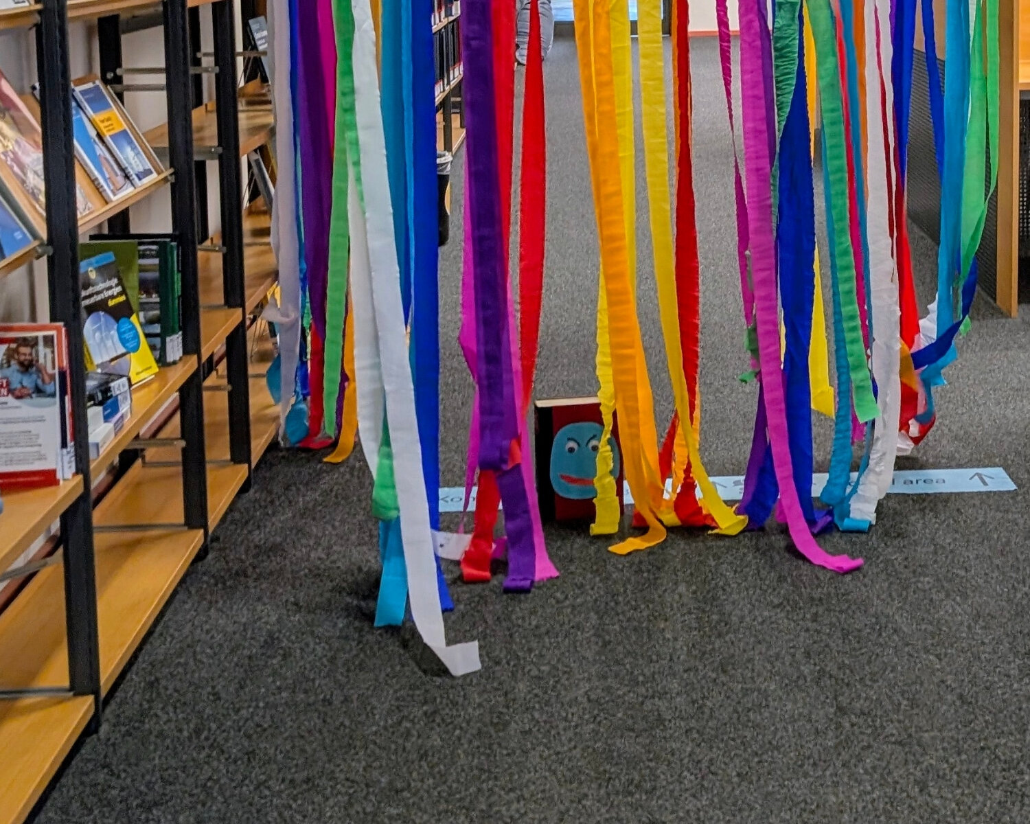 ein gebastelter Bücherwurm mit vielen bunten Papierstreifen auf dem Boden vor dem Bücherregal