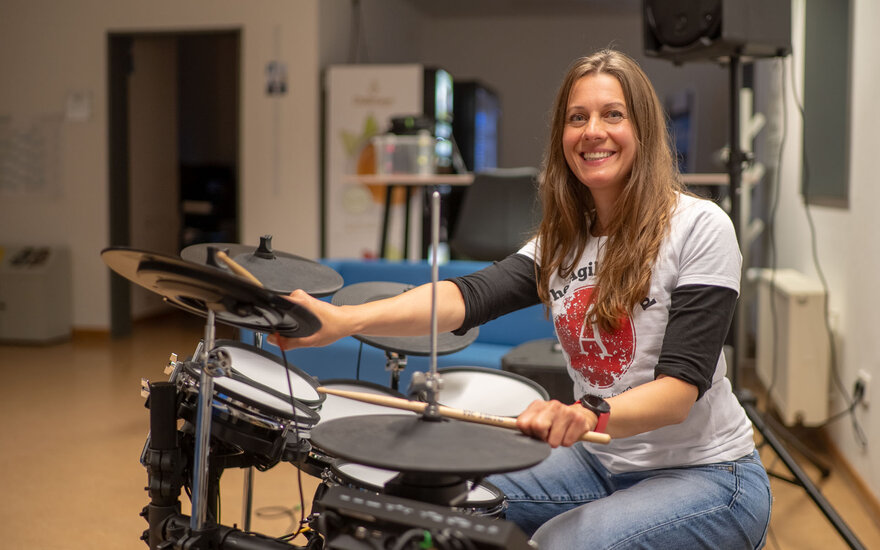 Professorin Bianca Weigand an ihrem Schlagzeug in die Kamera blickend
