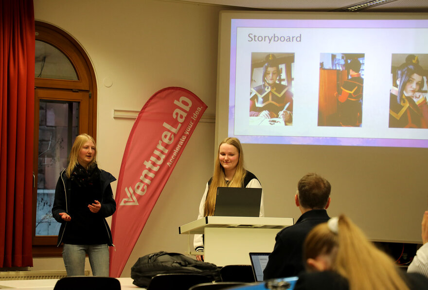 Zwei Studentinnen stellen ihre Idee am Pult vor ihren Komilitonen vor