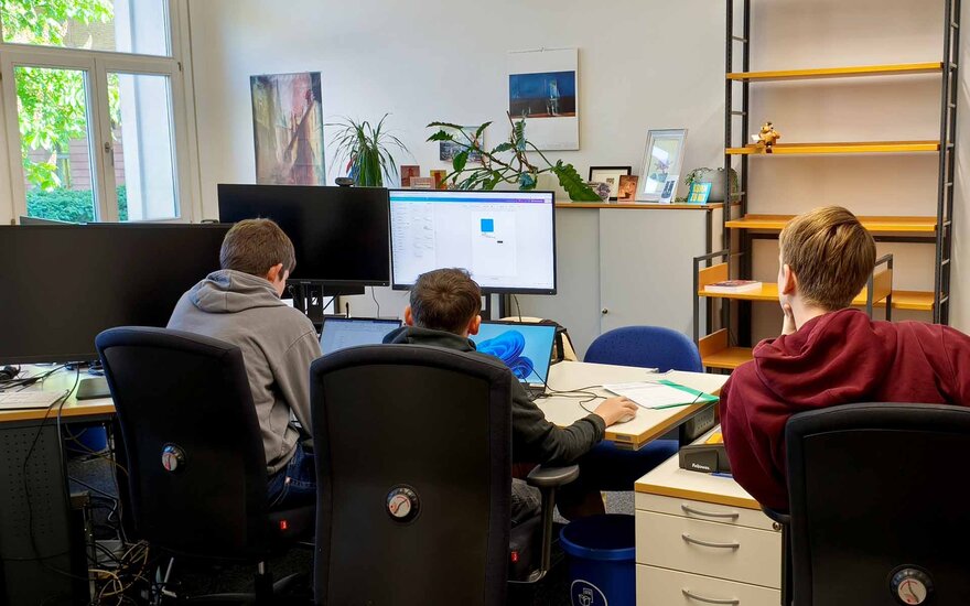 Drei Jungen sitzen vor einem Monitor in einem Büro und designen eine Memorykarte in Blau.