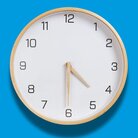 Runde Holzuhr mit weißen Ziffernblatt und Holzzeigern auf hellblauem Hintergrund