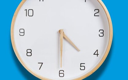 Runde Holzuhr mit weißen Ziffernblatt und Holzzeigern auf hellblauem Hintergrund