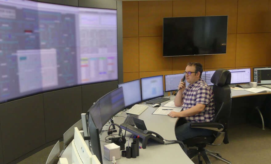 Hendrik Arend am Schreibtisch mit mehreren Monitoren und einem großen Bildschirm an der Wand