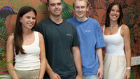 Vier Studierende, Christoph, Clarissa, Emilia und Marc, stehen lächelnd vor einer bunten Wand