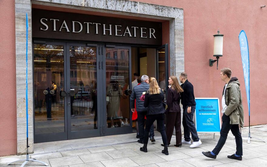 Fünf Personen laufen auf den Eingang des Theaters zu