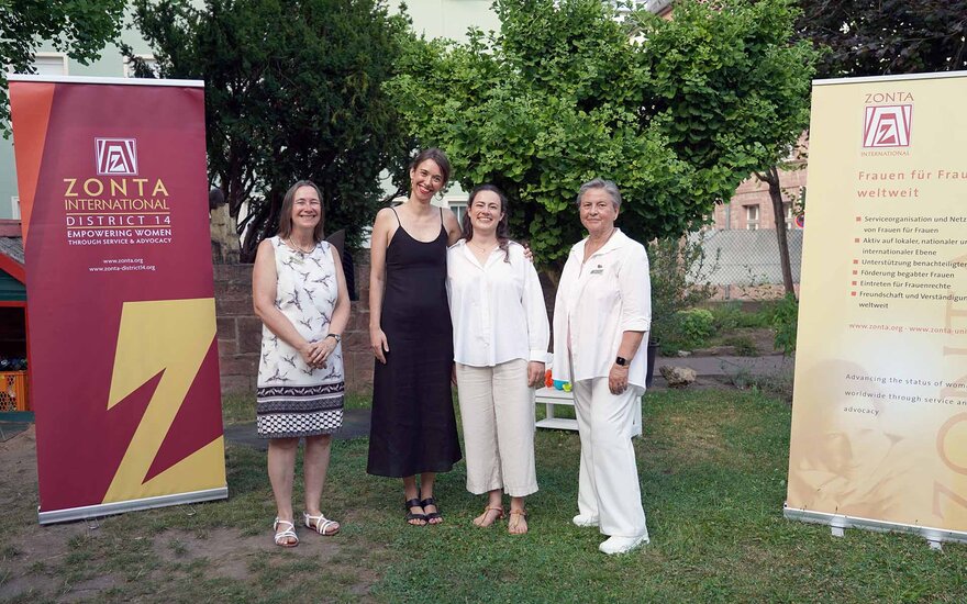 Studentin und Professorin stehen mit zwei Frauen aus dem ZONTA Club Aschaffenburg auf einer Wiese und rechts und links daneben ein rotes und ein gelbes ZONTA-Rollup