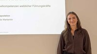 Frau mit langen dunkelblonden Haaren steht vor Leinwand mit Titel ihrer Promotion