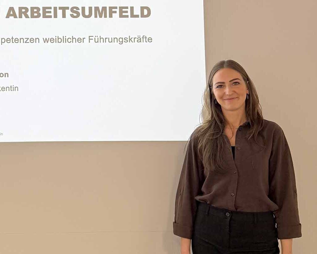 Frau mit langen dunkelblonden Haaren steht vor Leinwand mit Titel ihrer Promotion