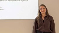 Frau mit langen dunkelblonden Haaren steht vor Leinwand mit Titel ihrer Promotion