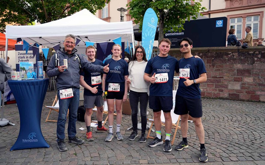 Mitglieder des TH-Laufteams stehen vor dem TH-Stand mit Bistrotisch und weißem Zelt