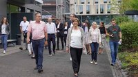 Präsidentin und Oberbürgermeister laufen mit Stadratsmitgliedern auf Weg vor Neubauten