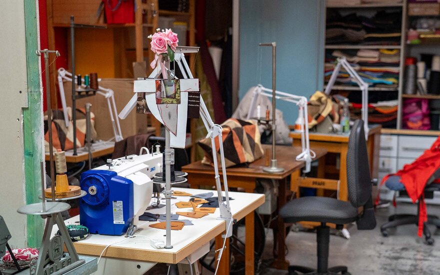 Nähwerkstatt des Vereins Gesta e. V.: Zu sehen sind drei Werkbänke mit Nähmaschinen, gefaltete Stoffe in den regalen im Hintergrund und Fetzen von Schnittmustern, die auf den Werkbänken zerstreut sind.