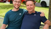 Vater und Sohn sitzen nebeneinander auf einer Bank am Campus