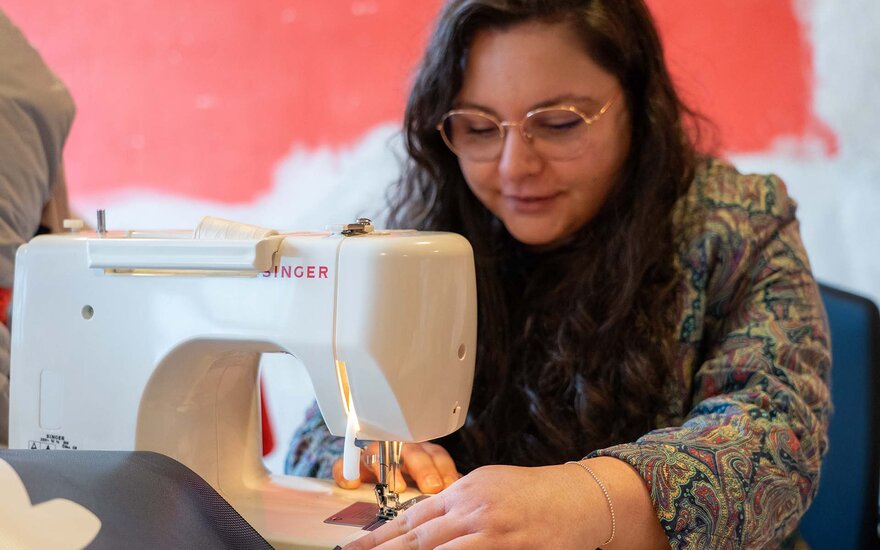 Alexandra Koch sitzt an einer Werkbank in der Nähwerkstatt des Gesta e.V. und näht an einem alten Werbebanner.