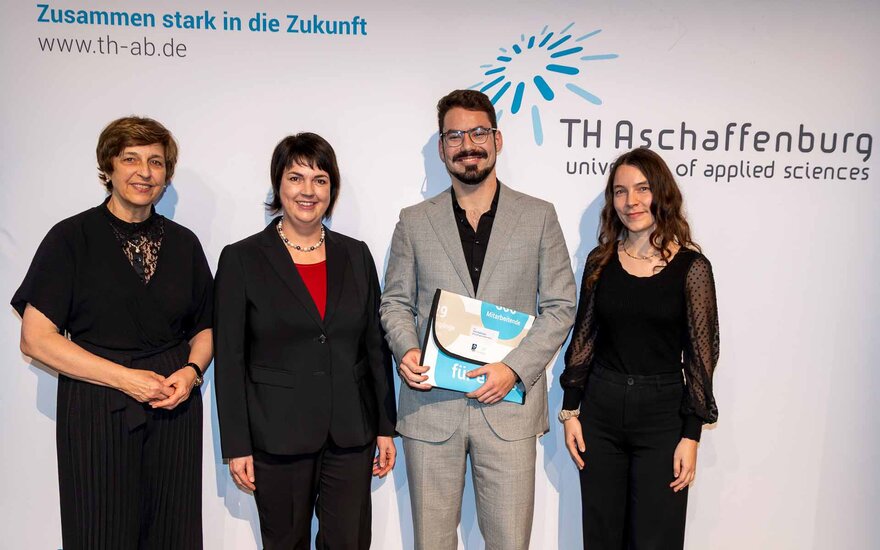 Junger Mann mit schwarzem Haar eingerahmt von drei Frauen in schwarzer Kleidung