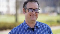 Hendrik Arend mit Brille im blauen Hemd vor der Campuswiese und TH-Gebäuden
