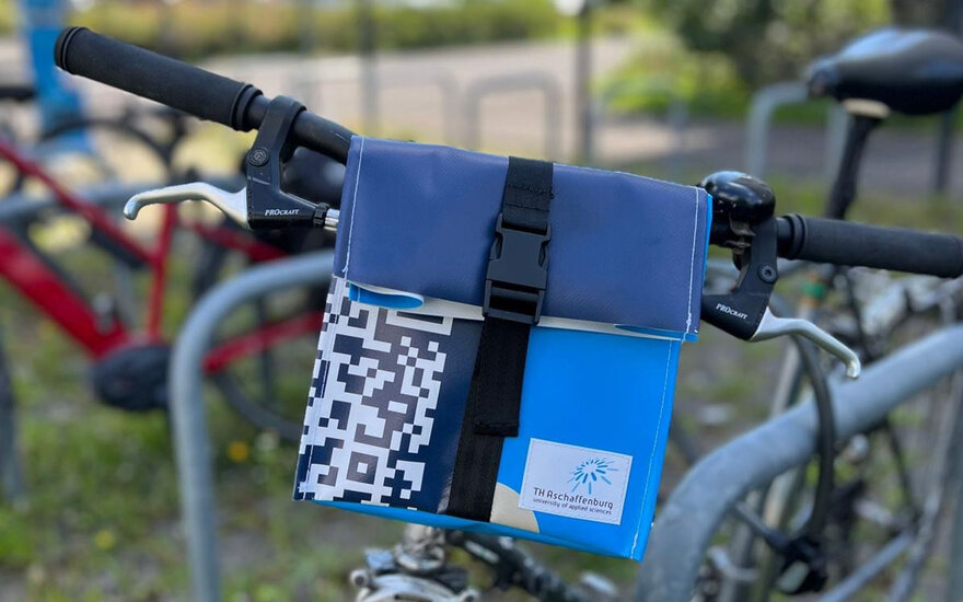 Eine Nahaufnahme von einem Upcycling-Produkt: Eine kleine, blaue Tasche, die an einem Fahrradlenker befestigt ist. Das Fahrrad befindet sich im Freien.