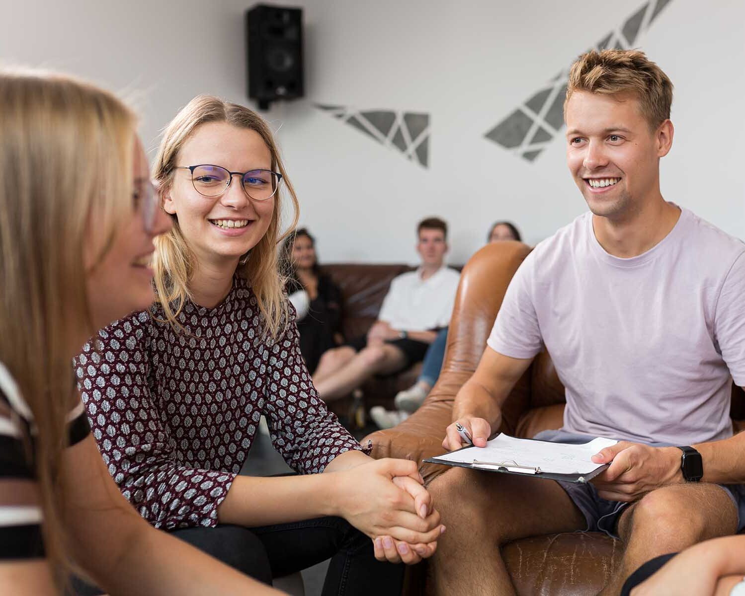 Drei Studentinnen und ein Student sitzen zusammen und unterhalten sich lächelnd