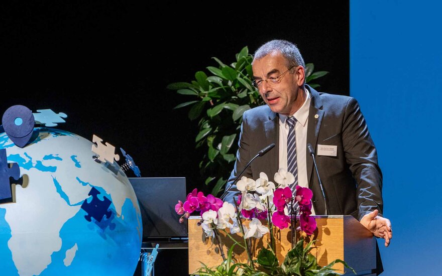 Älterer Mann mit dunkelgrauen Haaren und Brille im dunklen Anzug am Rednerpult