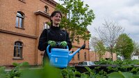 Eine junge Frau, die den Hochschulgarten gießt