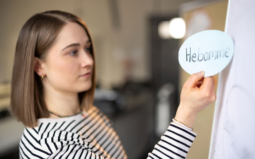 Eine Studentin schaut auf einer Karte mit dem Wort "Hebamme"