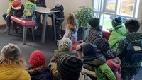 Kinder sitzen gemeinsam in einem Raum der Hochschule mit dem Rücken zur Kamera