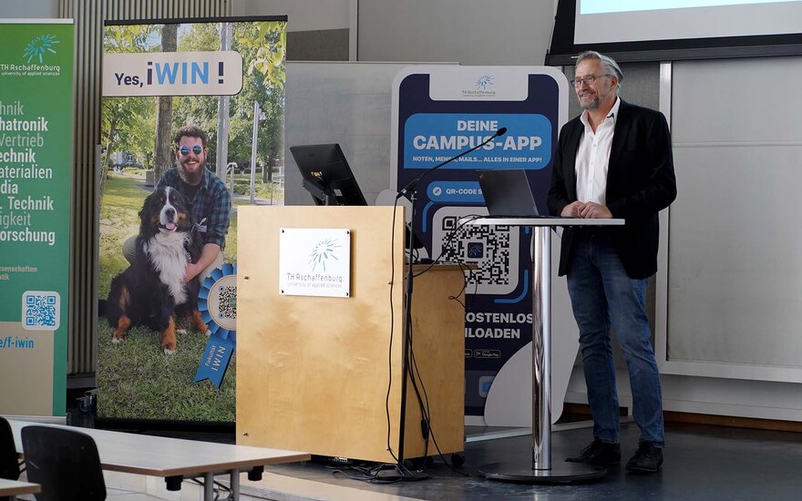 Professor Pietruschka am Rednerpult neben dem Banner der Fakultät IWIN