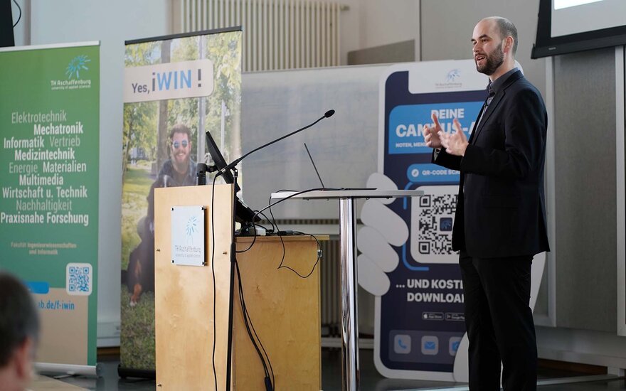 Professor von Kistowski am Rednerpult neben dem Banner der Fakultät IWIN