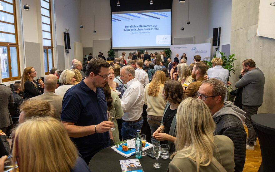 Mit Personen, die sich stehend unterhalten, gefüllte Aula