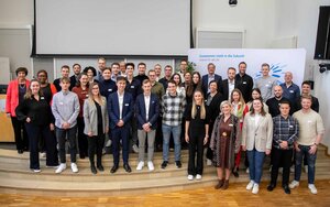 Die Stipendiatinnen und Stipendiaten des Deutschlandstipendiums zusammen mit ihren Fördernden vor der TH-Logo-Wand in der Aula