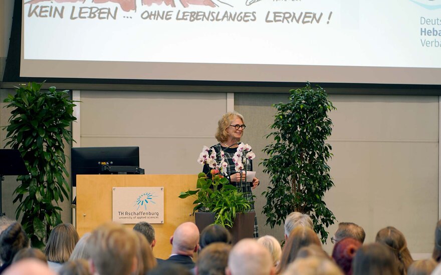 Frau spricht neben dem Rednerpult zum sitzenden Publikum